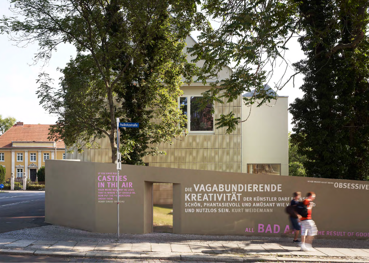Seitenansicht Neuwerk 11 (C) Christian Richters Seitenansicht des Grundstückes von der Peißnitzstraße aus. Glatte Mauer beigebraun mit Fensteröffnung aus Glas und verschiedenen Zitaten in Deutsch und Englisch. Hinter der Mauer ist das Gebäude sichtbar, jedoch leicht verdeckt von Bäumen