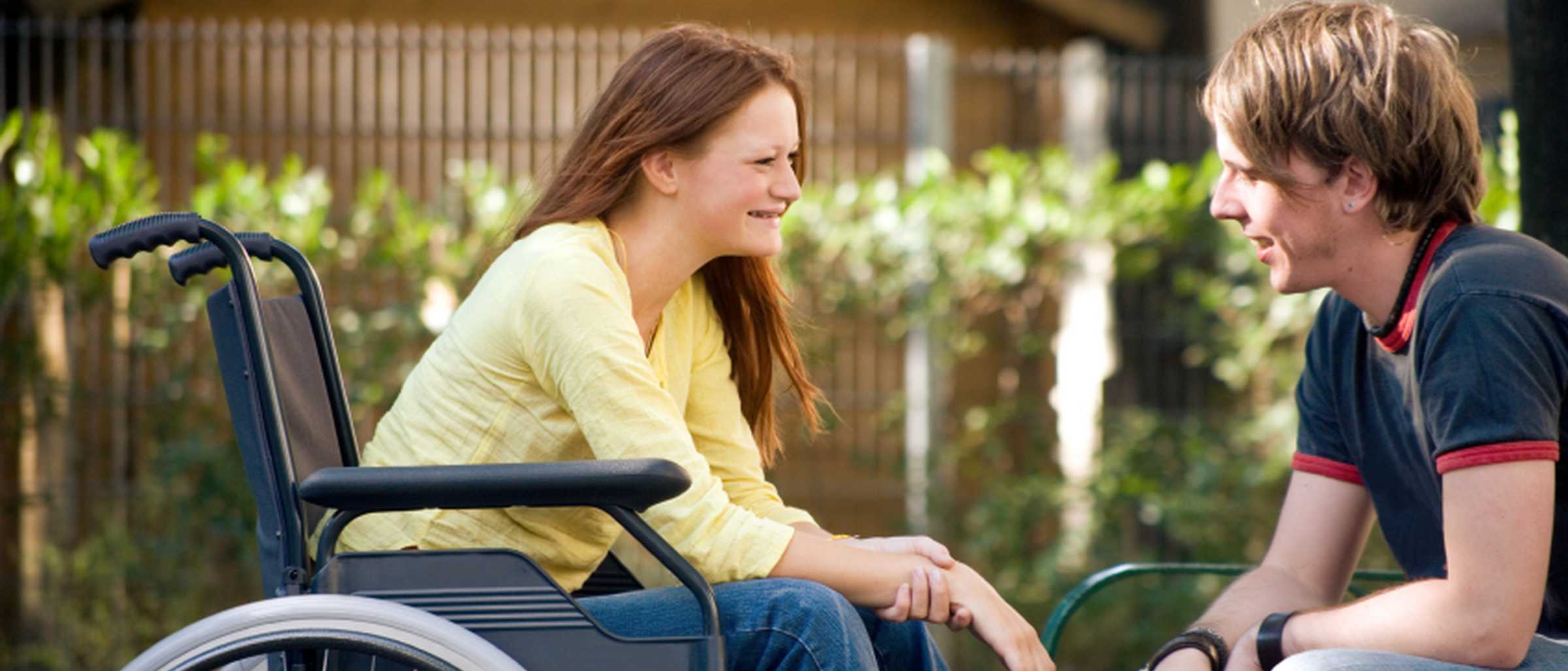 Junge Frau im Rollstuhl spricht mit einem jungen Mann