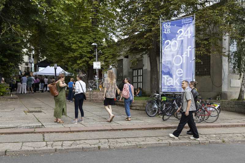 Eingangsbereich vom Schleifweg 8a mit Besuchern, die Richtung Eingang Volkspark gehen und der Ausstellungsflagge rechts im Bild zur Eröffnung der Ausstellung "Take Off 2024"