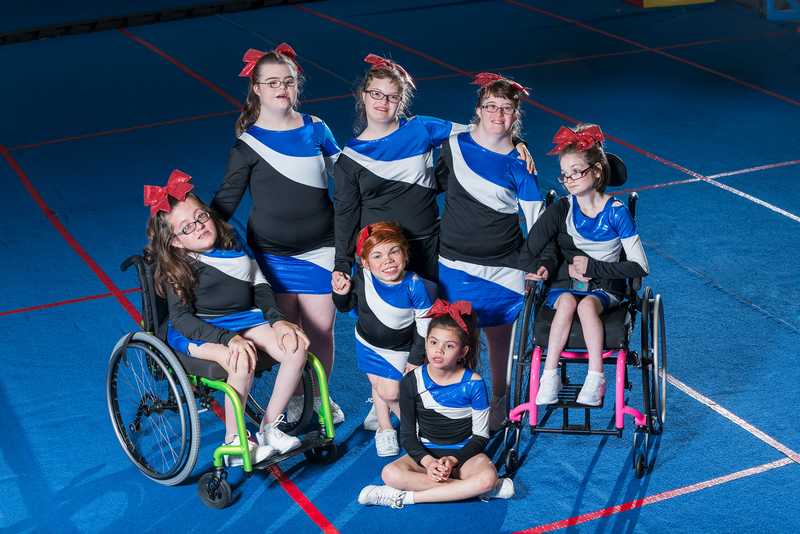 Sportlerinnen in blau-schwarzer Sportbekleidung mit unterschiedlichen Beeinträchtigungen auf einem blauen Sporthallenboden